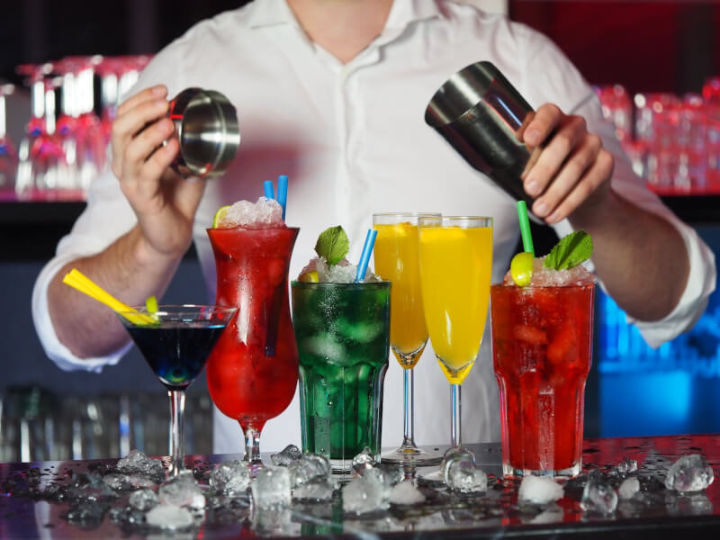 Person holding a shaker over a selection of colourful cocktails